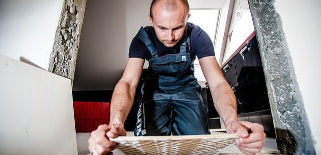burkolo A képen egy férfi burkoló látható munka közben. Egy járólapot helyez a földre.